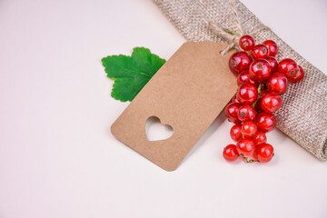 Blank kraft paper label with cut out heart and red currant berries on natural background