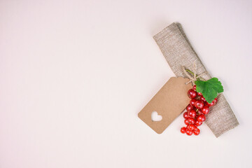 Blank kraft paper label with cut out heart and red currant berries on natural background