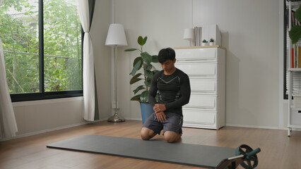 Asian male athlete sits on the floor to rest after completing a challenging workout at home.