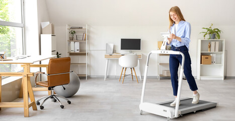 Young businesswoman with tablet computer training on treadmill in office