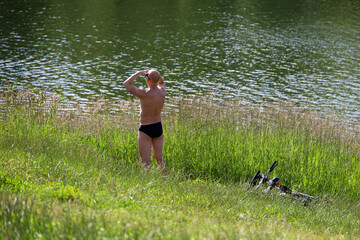 Man tan in a grass standing on a lake coast, summer leisure in hot weather