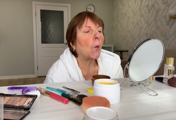 A beautiful senior woman is sitting at home and doing her make-up morning routine. Senior woman...