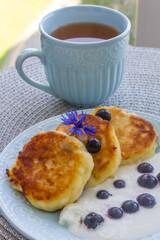 cheesecakes with sour cream, blueberries, cup of tea and cornflowers close-up for breakfast, photo...