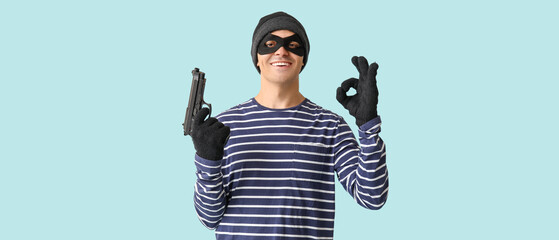Male thief with gun showing OK on blue background