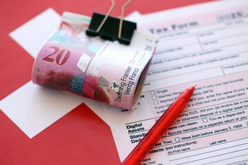 Swiss franc banknotes and tax form with pen. The current francs money bills lies on tax return form