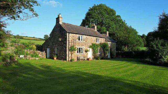Old stone cottage with lawn and trees in countryside