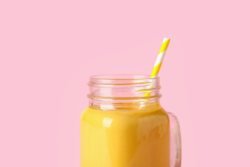Mason jar of tasty yellow smoothie with straw on pink background