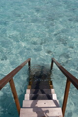 Wooden steps descending into crystal-clear turquoise water in the Maldives. A serene tropical...