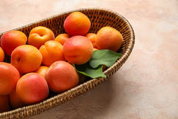 Wicker bowl with fresh apricots on beige background