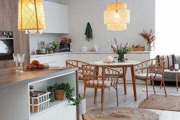 Interior of modern kitchen with dining table, island and glowing lamps