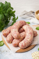 Wooden board with raw homemade sausages on light background