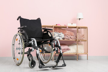 Modern empty wheelchair with shelving unit near pink wall