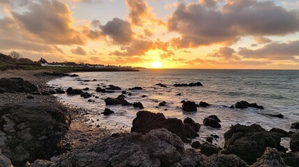 A breathtaking coastal sunset scene, showcasing a vibrant sky filled with clouds and the sun dipping below the horizon, casting a warm glow over the rocky shore and calm sea