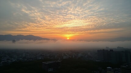 Fototapeta premium A breathtaking sunrise paints the sky with vibrant orange and gold hues, as a sea of fog blankets the cityscape nestled between distant mountains