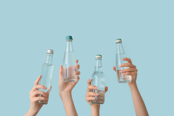Female hands with bottles of cold water on blue background
