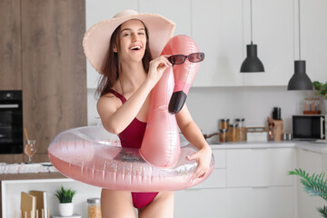 Young woman with sunglasses and swim ring ready for summer vacation in kitchen