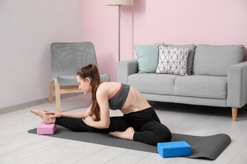 Sporty young woman stretching with yoga block at home