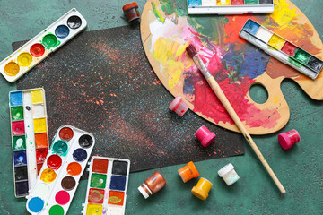 Composition with paints, palette, brush and paintings on green grunge background