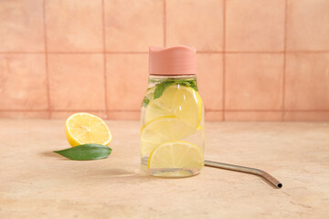 Sports bottle of infused water with lemon and mint on pink table