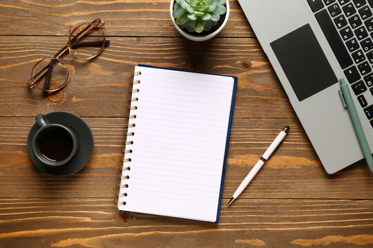 Notebook with laptop and cup of tasty coffee on wooden background