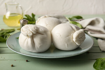 Plate of tasty Burrata cheese with basil on green wooden table