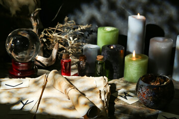 Witch's magic attributes with crystal ball of fortune teller and burning candles on dark table, closeup