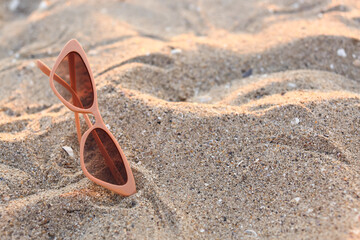 Stylish beige sunglasses on sand