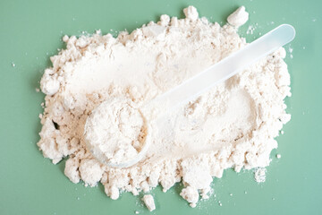 Scoop lies on scattered protein powder close-up view from above on green background.