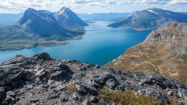 Panoramic view of a serene fjord nestled between majestic mountains, seen from a rocky peak.  The vibrant blue water contrasts with the earthy tones of the landscape