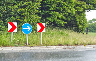 At a roundabout in Denmark, the signs show a red and white arrow and a white arrow in Blue sign