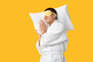 Portrait of handsome young man in bathrobe sleeping on pillow against yellow background