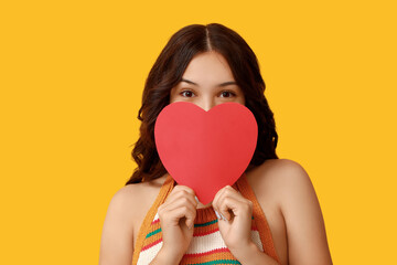 Beautiful young Asian woman with red paper heart on yellow background. Valentine's Day celebration