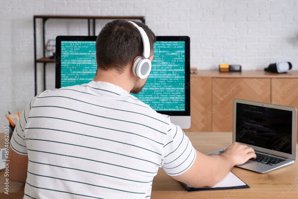 Poster male programmer working with computer and laptop in office, back view