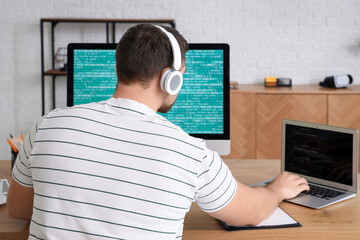 Male programmer working with computer and laptop in office, back view