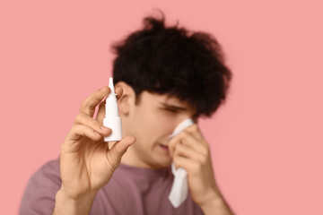 Young man with nasal drops and tissue on pink background. Allergy concept