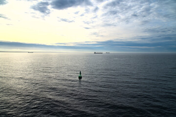 Green buoy in the calm sea at sunrise, ships on the horizon and dramatic sky