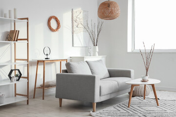 Interior of light living room with sofa, tables and willow branches in vases
