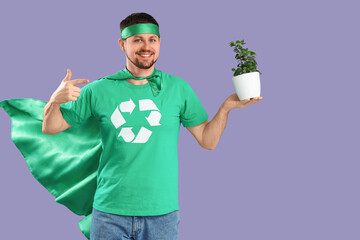 Young man dressed as eco superhero pointing at houseplant on lilac background. Ecology concept