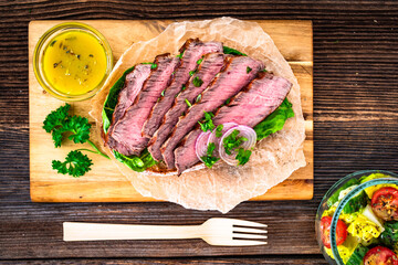 Takeaway sandwich with slices of grilled beef steak on wooden table	