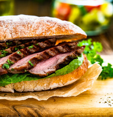 Takeaway sandwich with slices of grilled beef steak on wooden table	