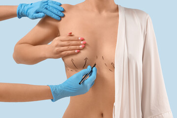 Plastic surgeon marking woman's breast on blue background, closeup