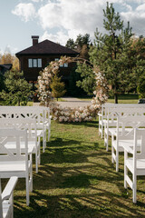 Rustic outdoor wedding ceremony with floral arch and white chairs in garden setting