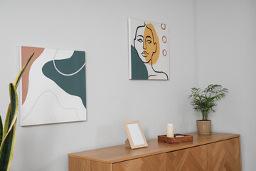 Interior of light room with chest of drawers, houseplant and pictures on wall