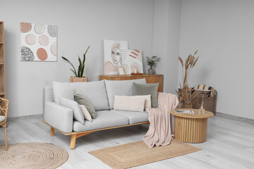Interior of light room with cozy sofa, coffee table and pictures on wall