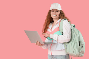 Happy female student with backpack pointing at laptop on pink background