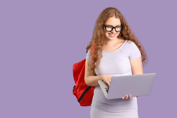 Happy female student with backpack and laptop on lilac background