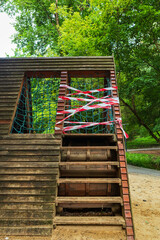 A damaged wooden structure on a playground is covered with red and white tape. Barricade warning tape  on a closed element of a playground