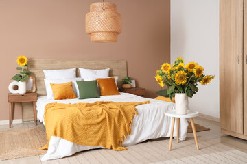 Stylish bedroom with big bed and vases of sunflowers bouquets on stool