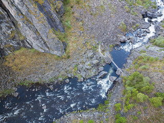 Aerial drone view of an impressive rocky canyon with a turbulent mountain river, a hiking trail,...