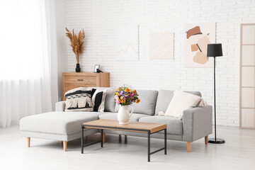 Cozy sofa and vase with wild flowers on coffee table in living room